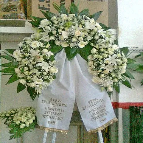 Μεγαλοπρεπές στεφάνι κηδείας με λευκά λίλιουμ, τριαντάφυλλα και επίσημη κορδέλα, έτοιμο για την τελετή αποχαιρετισμού.